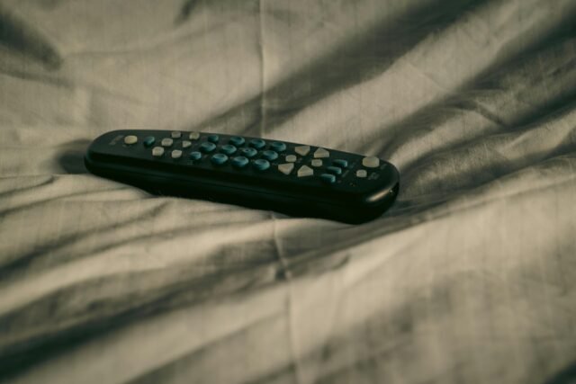 A remote control rests on wrinkled bed sheets, conveying a cozy and relaxed atmosphere.